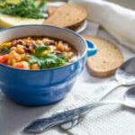 Hearty soup in a ceramic bowl with spoons and bread, illustrating soup packaging for meal train.