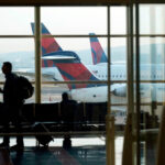 Passengers navigate airport terminal as planes are parked at gates, illustrating potential flight delays under Department of Transportation regulations.