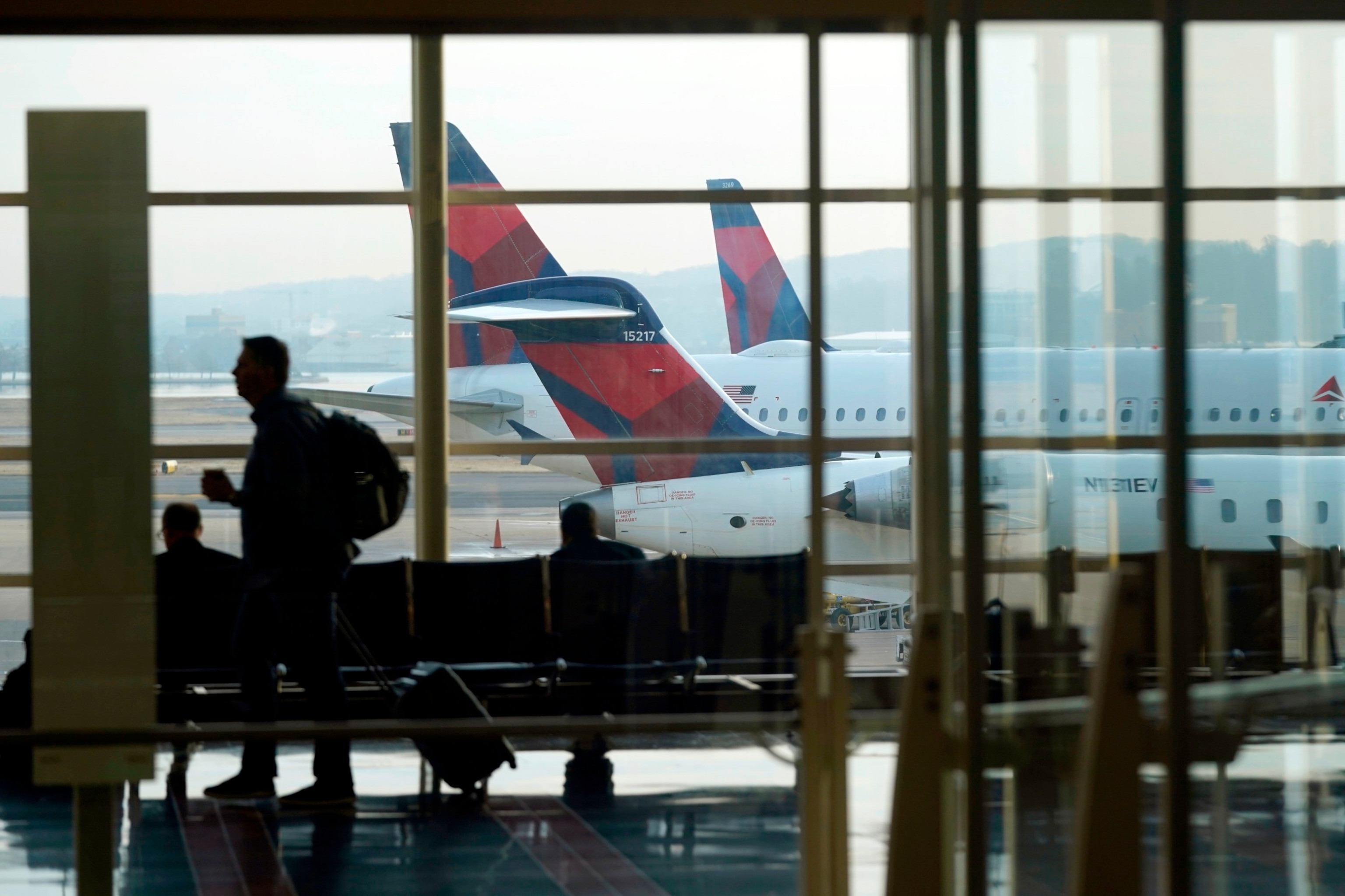 Passengers navigate airport terminal as planes are parked at gates, illustrating potential flight delays under Department of Transportation regulations.