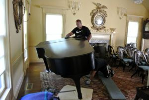 Once the piano lid is lowered and locked, Brian holds the piano while Sean removes the left front leg.