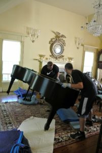 The piano is tilted and gently lowered onto the piano skid board.