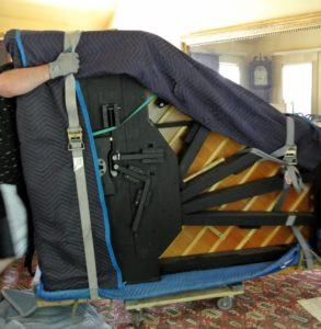 A moving dolly is carefully placed under the skid board and piano. At first glance it doesn