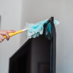 Preparing a flat screen TV for safe transport by dusting the screen to prevent scratches during the move.