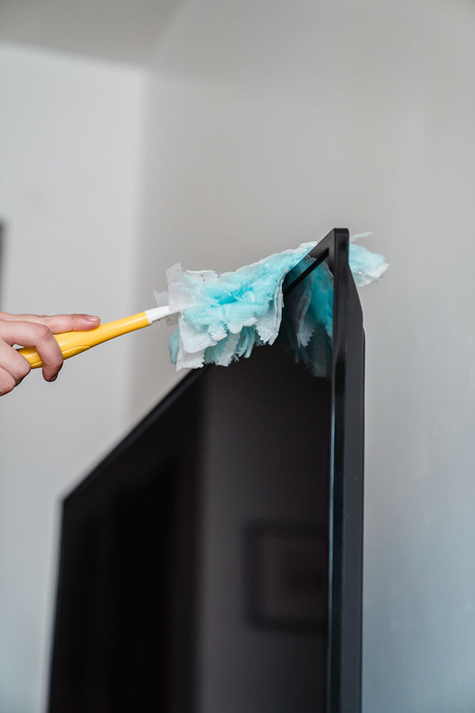 Preparing a flat screen TV for safe transport by dusting the screen to prevent scratches during the move.