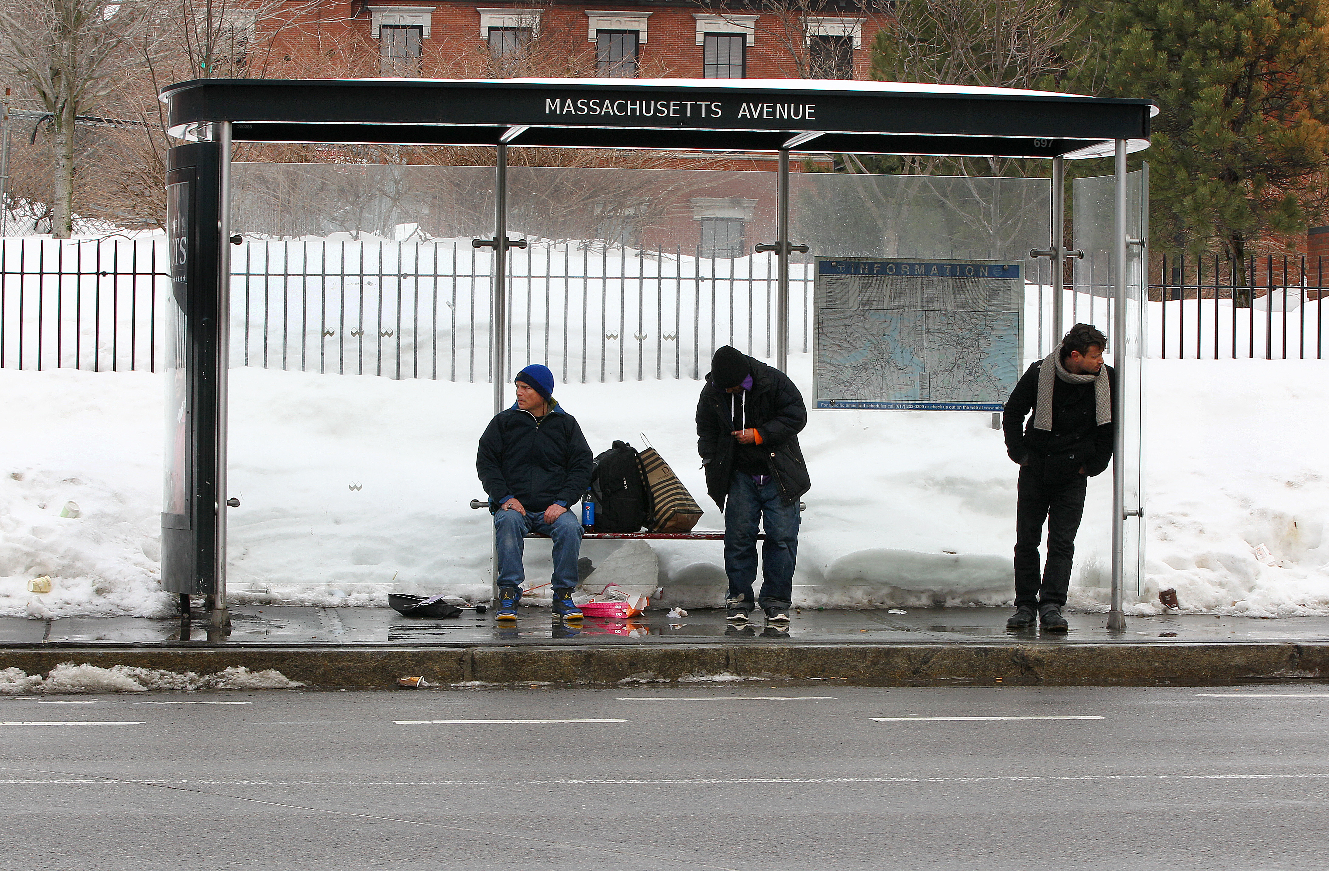 A lone person waiting at an empty bus stop, representing the often-inconvenient and underutilized nature of US public transportation.