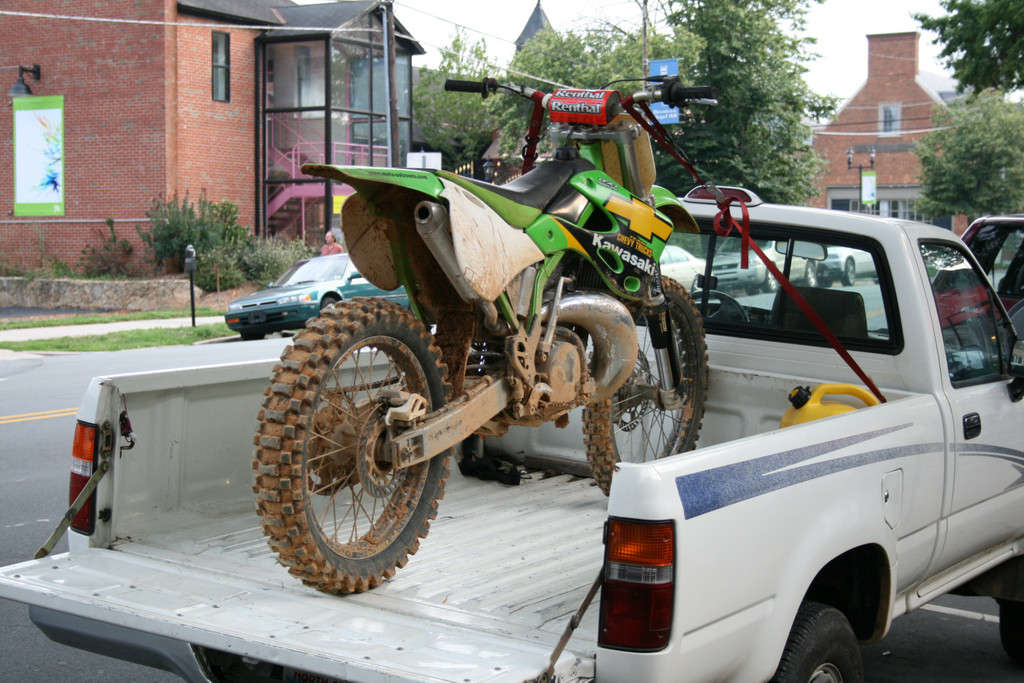 Dirt bike secured in pickup truck using wheel chock, straps, and bed liner for safe transport